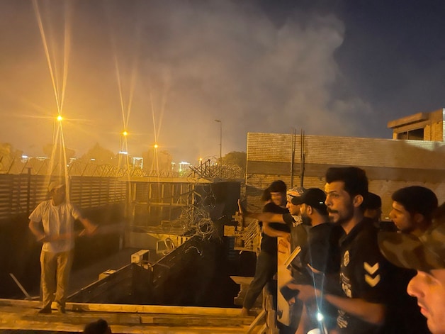 Honderden aanhangers van de invloedrijke Iraakse geestelijke Moqtada al-Sadr hebben donderdag de Zweedse ambassade in Bagdad bestormd en in brand gestoken. Op deze foto zijn mensen te zien die op het dak van een naastgelegen gebouw staan.