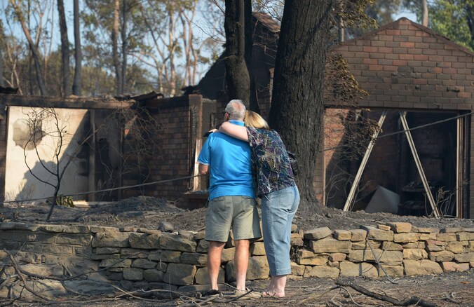 Een echtpaar aanschouwt de resten van zijn uitgebrande woning in Winmalee, in de Blue Mountains ten westen van Sydney.
