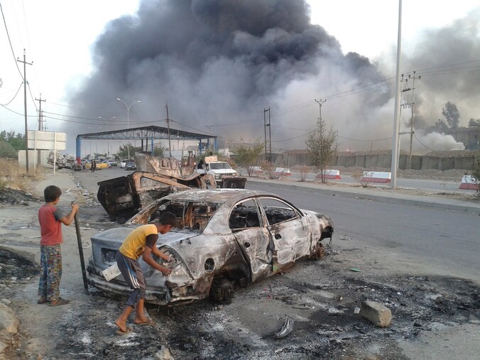 Kinderen staan naast een uitgebrande auto in Mosul, de noordelijke Iraakse stad die in handen is gevallen van ISIS.