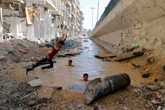 Kinderen in Aleppo duiken in een krater die volgens activisten het gevolg is van de ontploffing van een vatenbom.