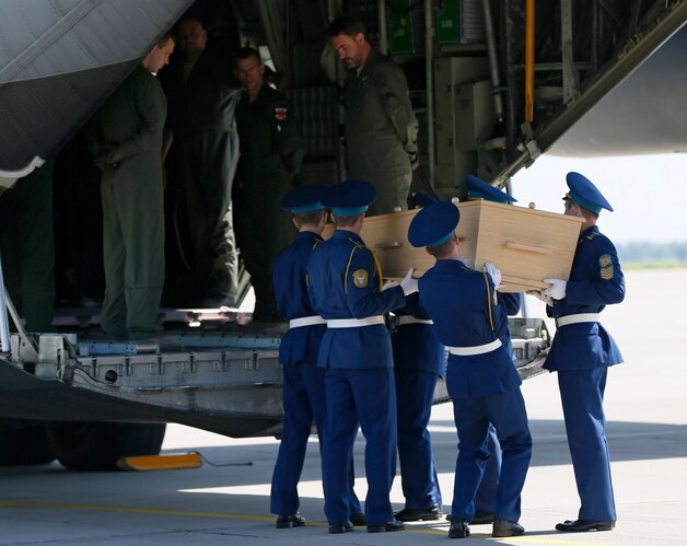 Een kist met één van de lichamen wordt in een militair toestel gezet.