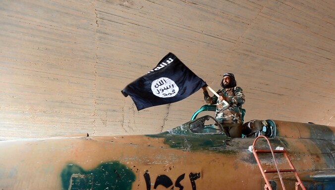 Een IS-strijder poseert trots met een in beslag genomen jet van het Syrische regeringsleger.