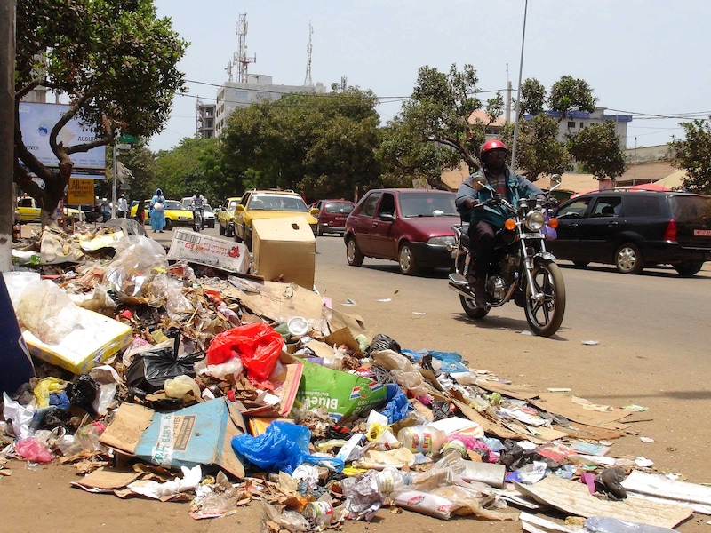 Een motorrijder passeert een berg afval in de hoofdstad Conakry.