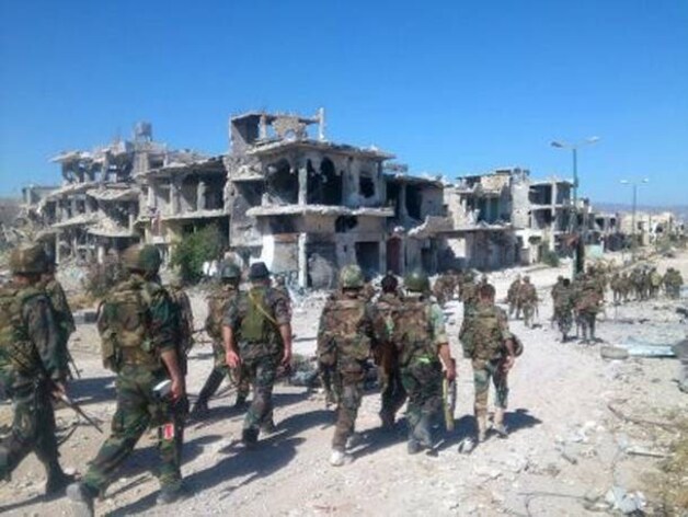 Syrische soldaten paraderen door het zwaar verwoeste Qusair, nabij de Libanese grens.