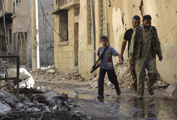 Een kind draagt een kalasjnikov in Syrië.
