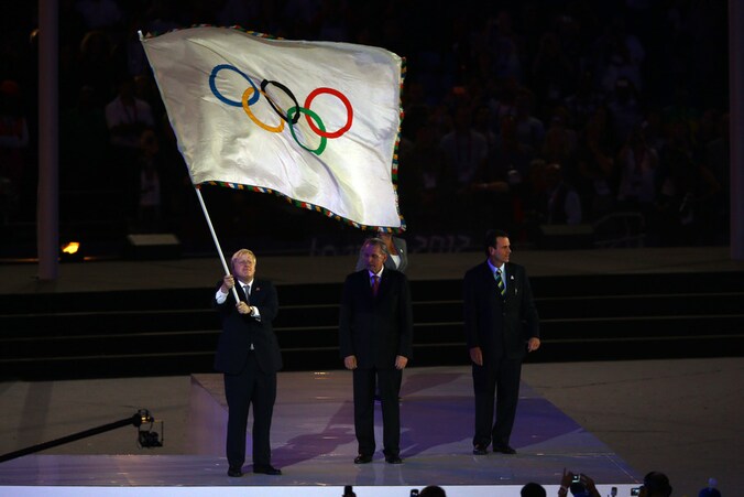 Boris Johnson zwaait vier keer met de olympische vlag alvorens die door te geven.
