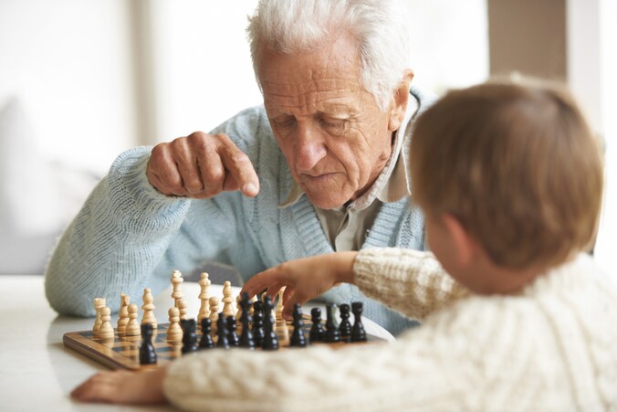 Een oude man speelt een schaakpartij met zijn kleinzoon. Het brein van oude mensen werkt trager omdat het meer informatie moet verwerken.