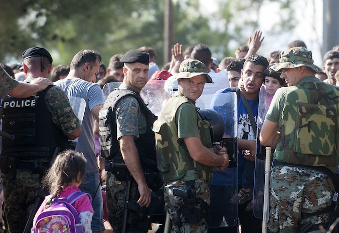 Migranten wachten bij een rij agenten aan de Macedonische grens.