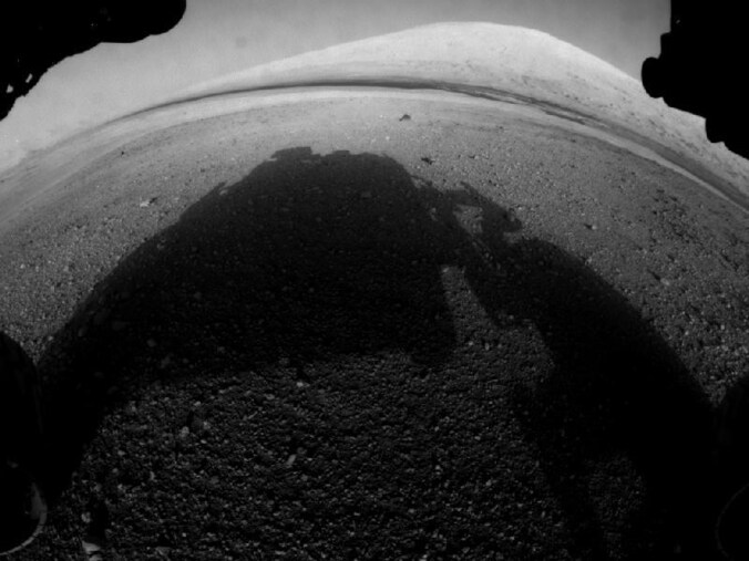 Een schaduw van de Curiosity, met in de verte de 5,5 kilometer hoge Mount Sharp.