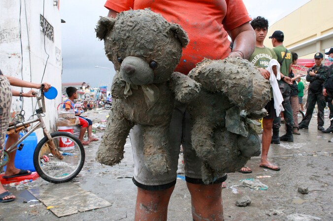 Een vrouw draagt de knuffels van haar dochter in het zwaar getroffen Tacloban.