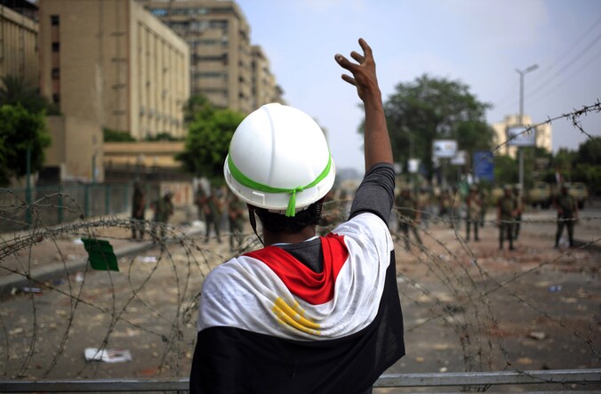 Een aanhanger van Mursi maakt gebaren richting Egyptische soldaten die het hoofdkwartier van de Republikeinse Garde in Caïro bewaken.