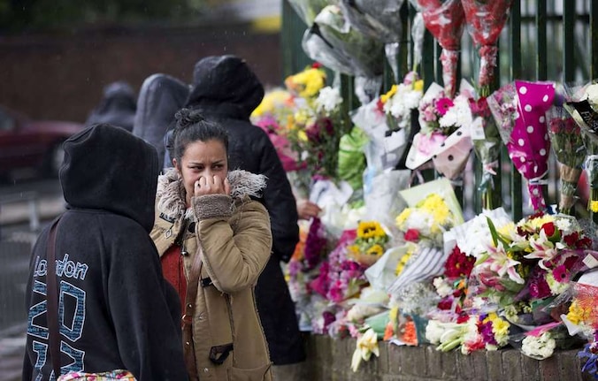Een vrouw kijkt naar de bloemen die achtergelaten zijn op de plek waar Lee Rigby werd vermoord.