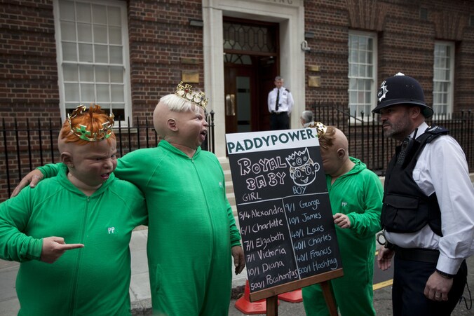 Medewerkers van een gokkantoor poseren met babymaskers voor een bord waarop potentiële namen voor de baby van Kate en William staan.