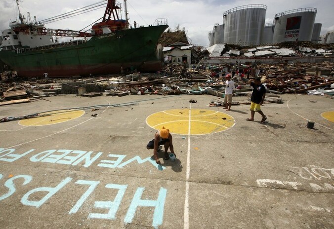 Een Filipijnse vrouw schildert een oproep voor help op straat in het zwaargehavende Tacloban.