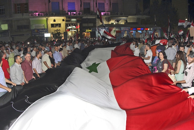 Aanhangers van de Syrische president Assad dragen een enorme vlag tijdens een bijeenkomst in Damascus.
