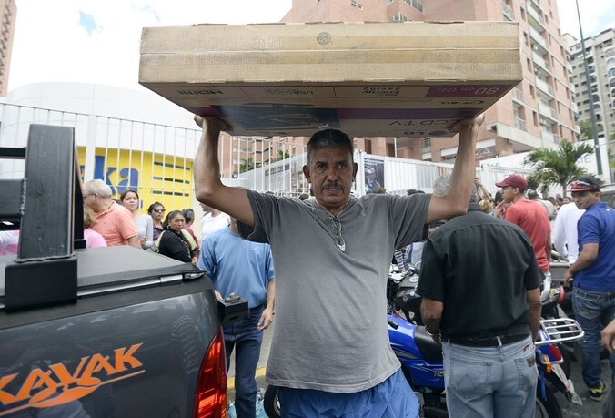 Een man tilt een lcd-tv boven zijn hoofd nadat hij heeft geshopt bij een vestiging van de elektronicaketen Daka in de Venezolaanse hoofdstad Caracas.