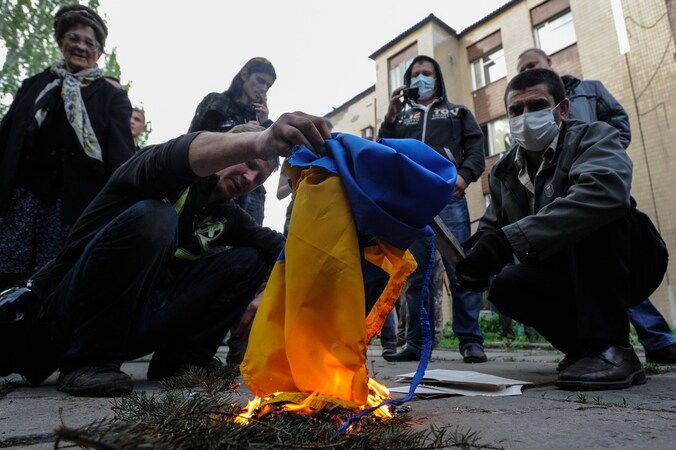 Pro-Russische demonstranten steken in de stad Donetsk de Oekraïense vlag in brand.