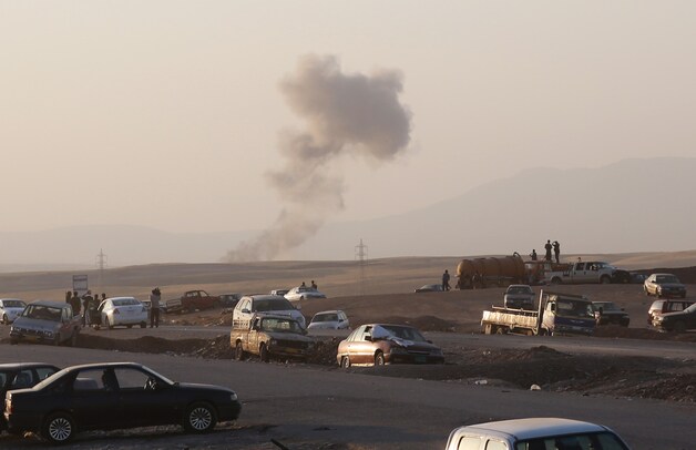 Rookpluimen na een Amerikaans bombardement op IS-stellingen. Koerdische inwoners van Erbil kijken toe.