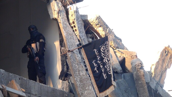Een strijder van al-Nusra naast de vlag van de groepering in een ingestort gebouw, net als IS getroffen door Amerikaanse luchtaanvallen.