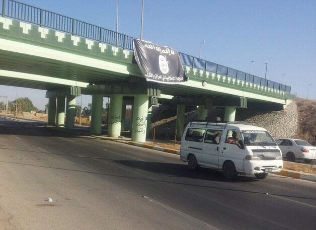 Een busje passeert een viaduct met een vlag van de Islamitische Staat in de Noord-Irakese stad Mosul.