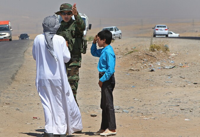 Een Koerdische soldaat helpt een Irakese man bij een controlepost tussen Mosul en Irbil.