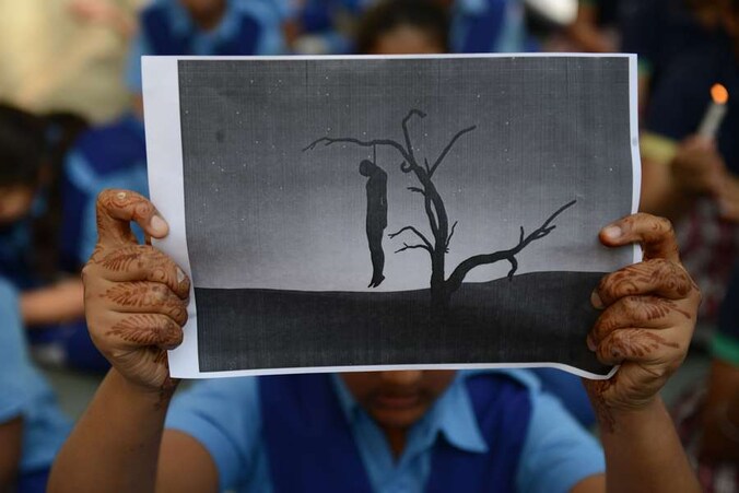 Een schoolmeisje houdt een papier met een man hangend aan een boom op tijdens een protest tegen verkrachtingen in haar land.