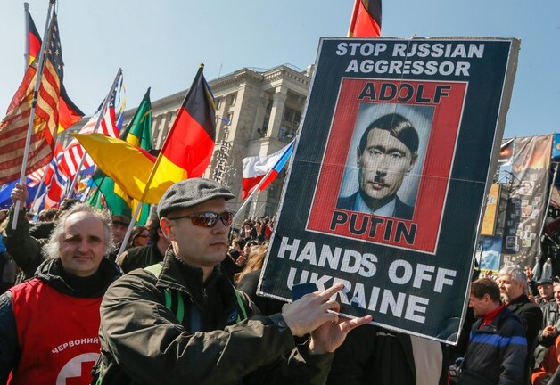 Deze demonstrant in Kiev vergelijkt de Russische president Poetin met Adolf Hitler.
