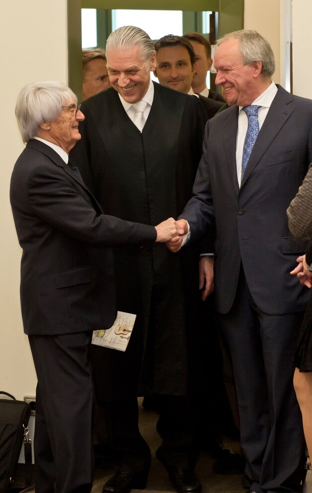 Ecclestone (l), in het gezelschap van zijn advocaat Sven Thomas, schudt de hand met procureur Manfred Nötzel.