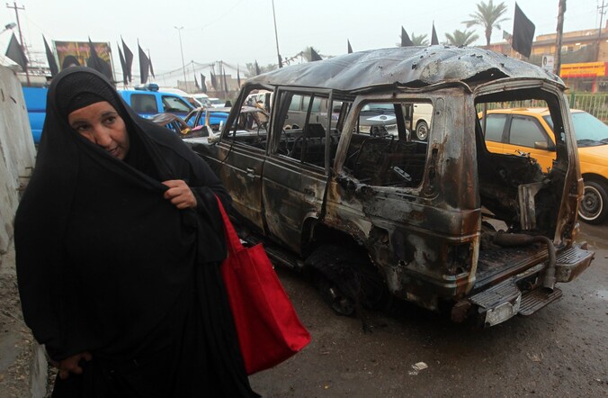 Een vrouw wandelt voorbij het wrak van een bomauto in Bagdad eind november.