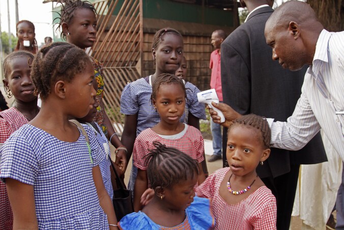 Een gezondheidswerker in Guinee controleert of schoolkinderen geen koorts hebben.