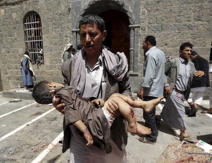 Een man draagt een gewond kind de moskee in Sanaa uit.
