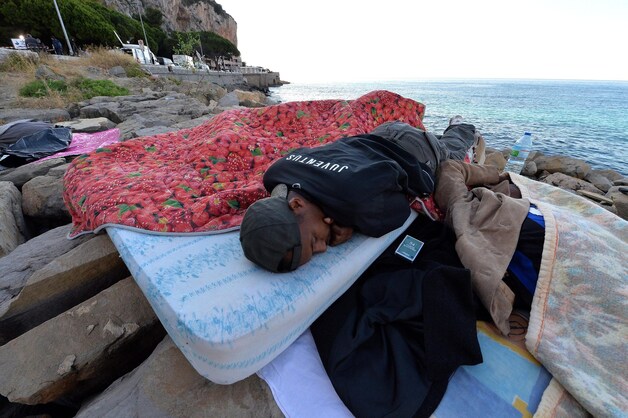 Een vluchteling slaapt op de rotspartijen in Ventimiglia.