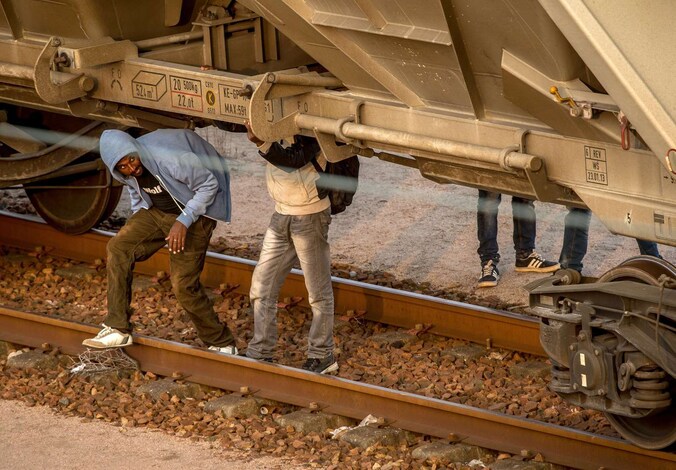 Migranten verbergen zich onder een goederentrein die via de Eurotunnel naar Engeland gaat.