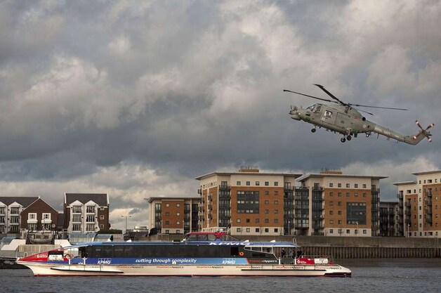 Een Royal Navy Lynx-helikopter vliegt boven een passagiersferry op de Theems.