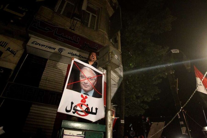 Een betoger toont een foto van Shafiq met een rood kruis over.
