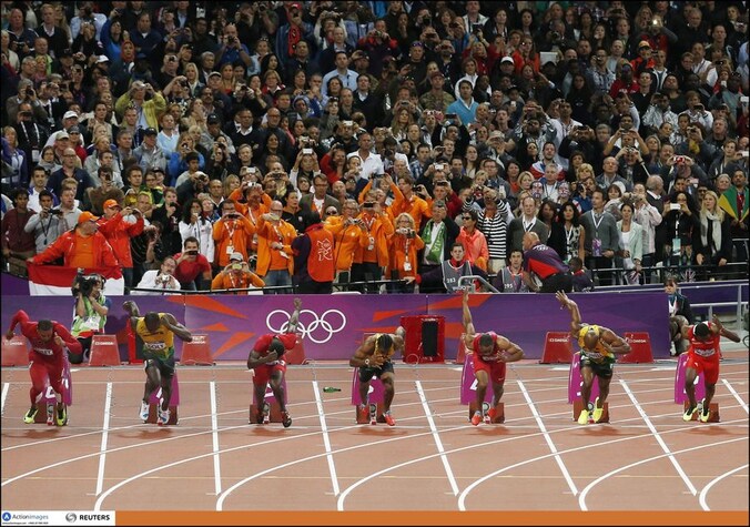 De start van de 100m-finale. Achter de lopers ligt een fles, de Nederlandse delegatie, met daarbij Edith Bosch, staat in de buurt.