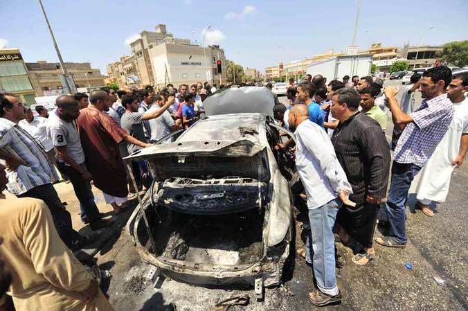 Omstanders bekijken het wrak van een auto na ontploffing van een autobom in Benghazi, dinsdag.