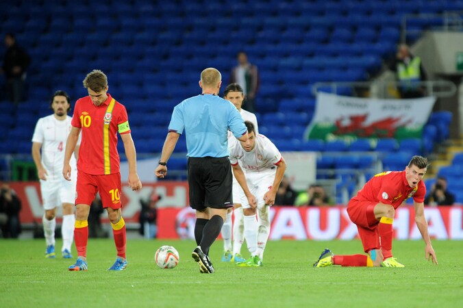 Gareth Bale (rechts) in het shirt van Wales komt overeind na een harde tackle.