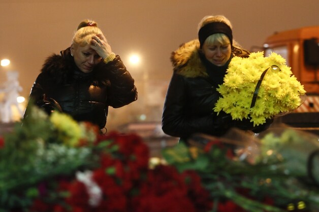 Twee vrouwen leggen bloemen nabij het treinstation waar zondag 17 mensen omkwamen.