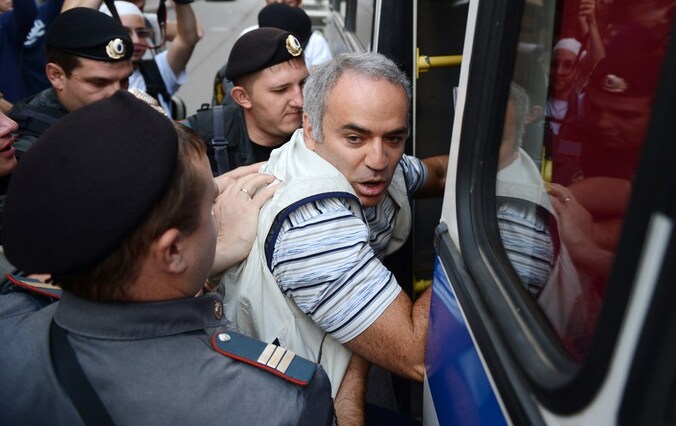 Kasparov wordt een politiebusje ingeduwd.
