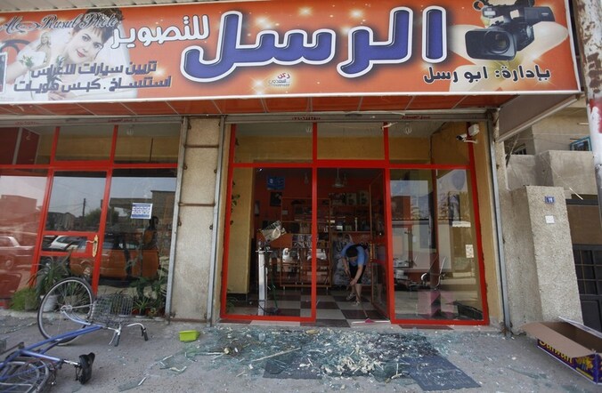 Een winkelier in Bagdad veegt glasscherven op, nadat de winkelruit bij de bomaanslag is gesneuveld.