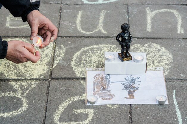 Een man ontsteekt een kaars naast een beeldje van Manneken Pis op het Beursplein in Brussel, de dag van de aanslagen.
