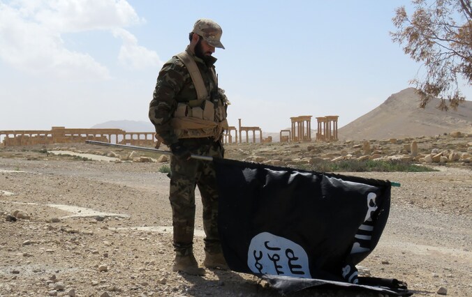Een Syrische soldaat houdt een IS-vlag vast na de herovering van de stad.