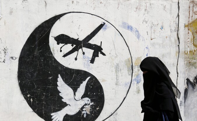 Een Jemenitische vrouw wandelt voorbij graffiti waarin de Amerikaanse droneaanvallen op Jemen worden aangeklaagd.