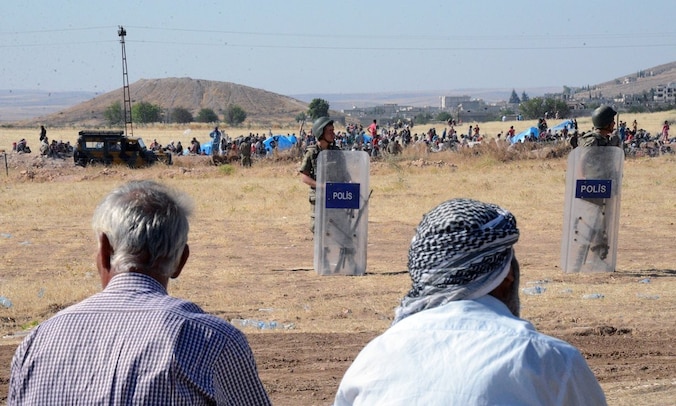 Turkse grenswachters en Syrische vluchtelingen die de grens willen oversteken.