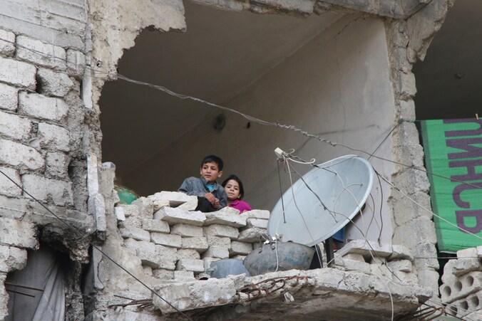 Kinderen kijken naar buiten in een huis dat zwaar geleden heeft onder het oorlogsgeschut in Aleppo.