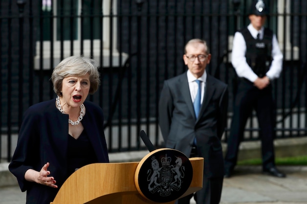 Theresa May geeft haar eerste speech als premier, met op de achtergrond haar echtgenoot Philip.