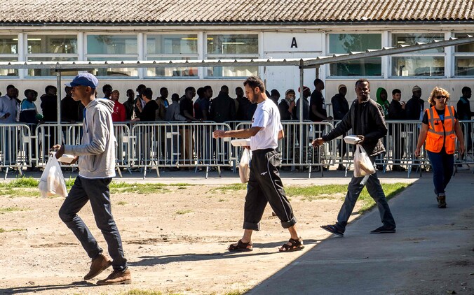 Asielzoekers staan in de rij voor de voedselbedeling door 'Vie Active' in het kamp in Calais.