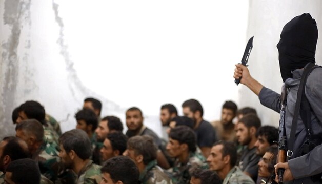 Een IS-strijder bewaakt gevangen genomen soldaten van het Syrische leger bij een ingenomen luchtmachtsbasis bij Raqqa.