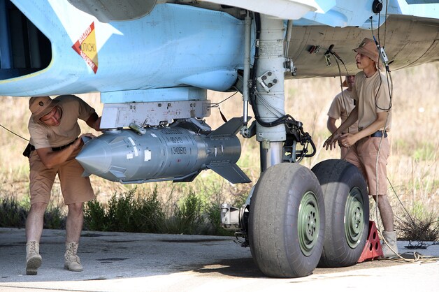 Russische militairen bevestigen een satellietgestuurde bom onder een SU-34 gevechtsvliegtuig op de luchtmachtbasis van Hmeimim in Syrië.